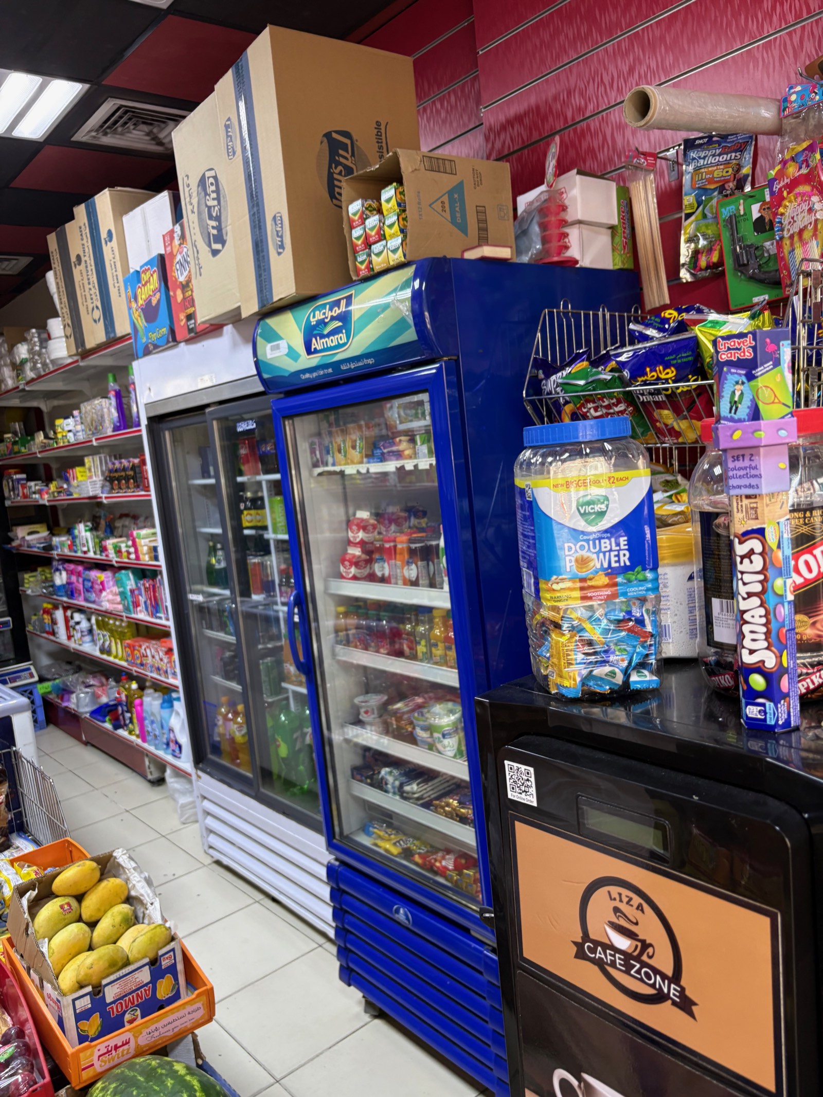 A neighbourhood grocery shop (bakkala) in the UAE, its shelves and fridge stocked with drinks, snacks and fresh produce.
